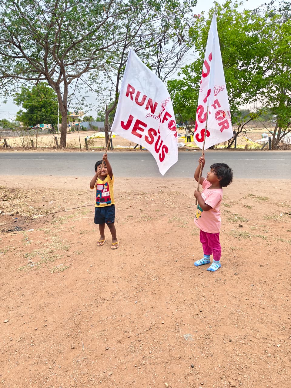 Children holding Run for Jesus flags outdoors.